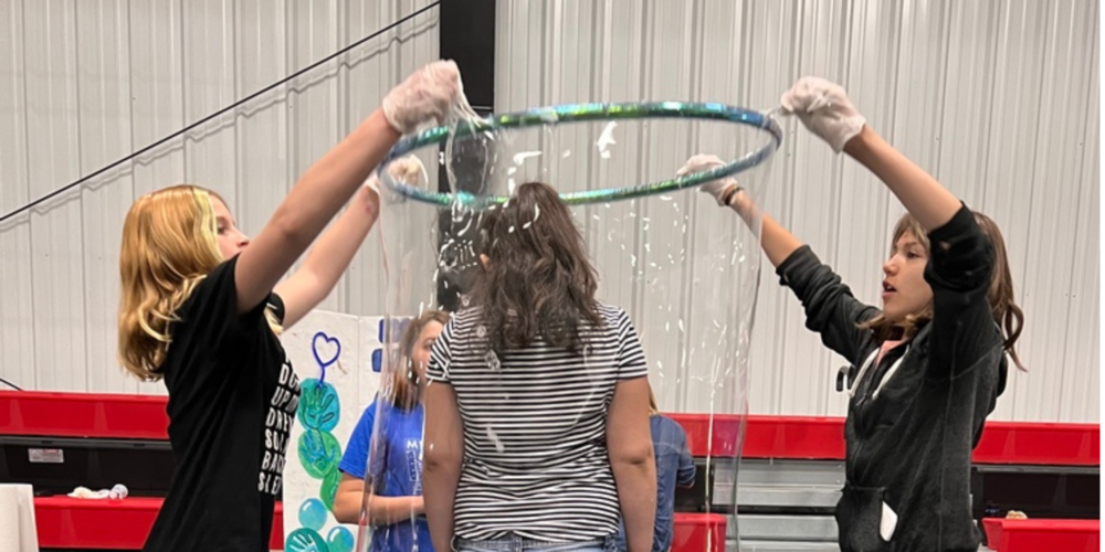 two students encasing another in a giant bubble using a hula hoop